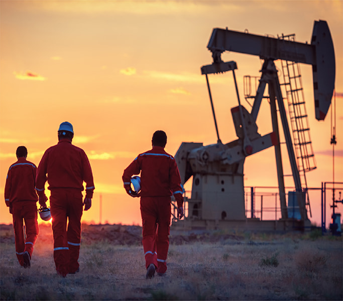group of production and exploration engineers discussing operations on an oil field, with drilling equipment and storage tanks visible in the background.